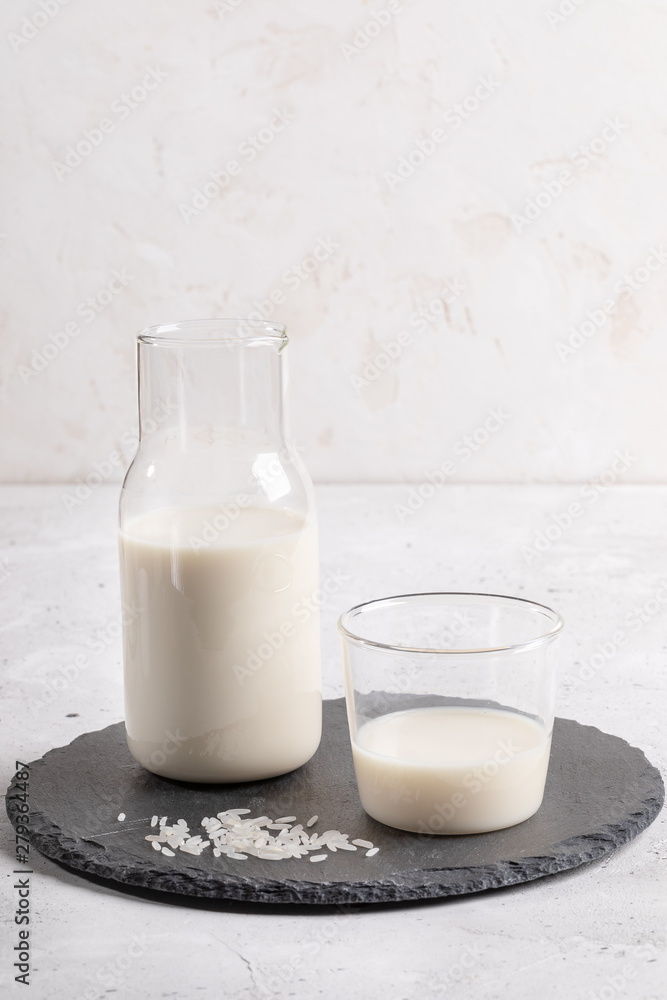 Drinking glass and glass bottle with healthy rice milk on round shale board on white background. Drinking glass and glass bottle with healthy rice milk on round shale board on white background.