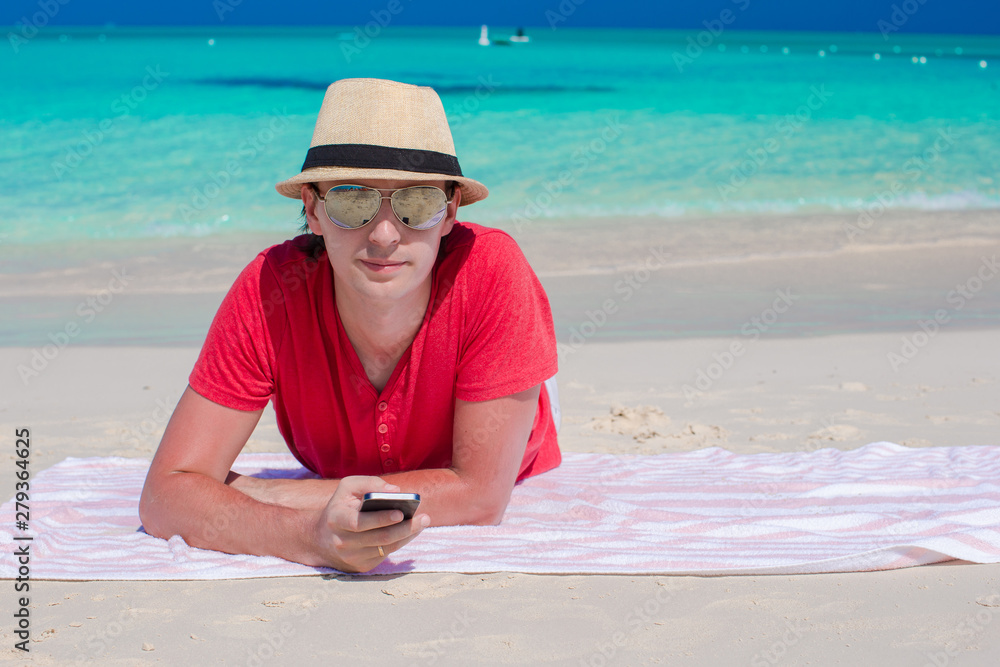 Young guy with cellphone on tropical white beach