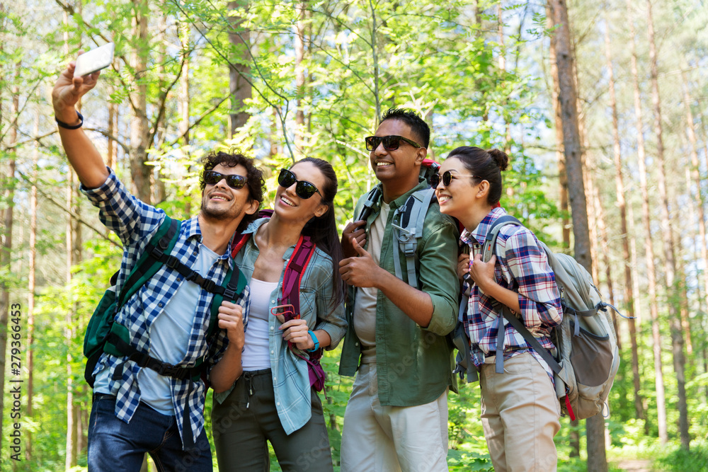 travel, tourism, hike and people concept - group of friends with backpacks taking selfie by smartphone in forest travel, tourism, hike and people concept - group of friends with backpacks taking selfie by smartphone in forest
