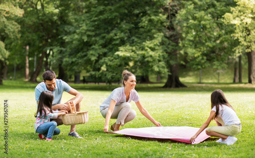 family, leisure and people concept - happy mother with daughter laying down picnic blanket on grass in summer park