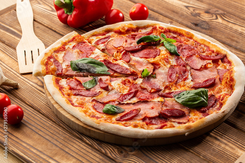 Pizza with ham , hot sausages, salami and mozzarella on wooden background close up. Italian cuisine. Pizza with prosciutto and salami on wooden table. top view.