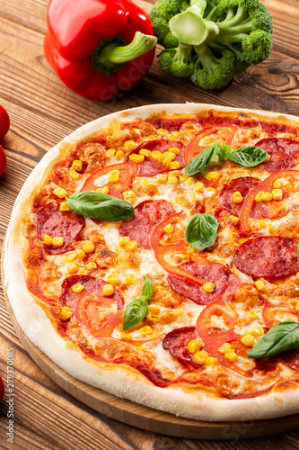 Delicious hot homemade pizza on the wooden table. Pizza - Fresh homemade pizza with pepperoni, cheese and tomato sauce, tomatoes, sweet corn and basil with copy space.