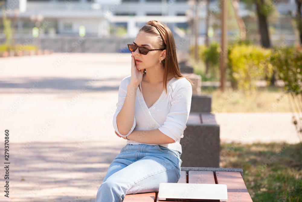 Beautiful woman sitting on a park bench using a laptop. Beautiful woman sitting on a park bench using a laptop.