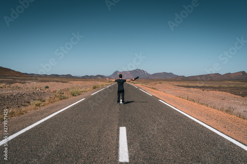 Guy with a camera spreads his arms looking the landscape, incredible road in Morocco