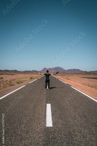 Guy with a camera spreads his arms looking the landscape, incredible road in Morocco