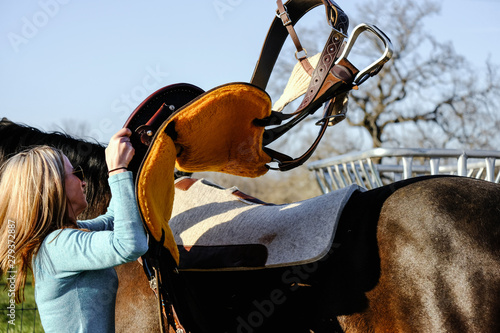 Woman riding horse, putting saddle on in action.