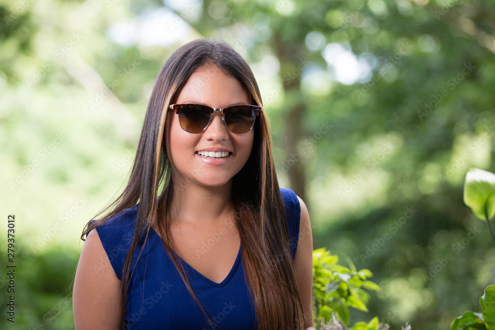 Closeup portrait of beautiful lady at window with nature as background. She is smiling to the camera. She has long and smooth hair, bright eyes, nice smile and sun tanned skin. She is wearing sunglass Closeup portrait of beautiful lady at window with nature as background. She is smiling to the camera. She has long and smooth hair, bright eyes, nice smile and sun tanned skin. She is wearing sunglass