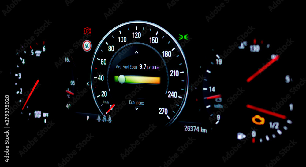 Side view of modern car dashboard with speedometer, tachometer, odometer, car's temperature gauge and check engine. Selective focus of average fuel economy consumption display on car instrument panel.