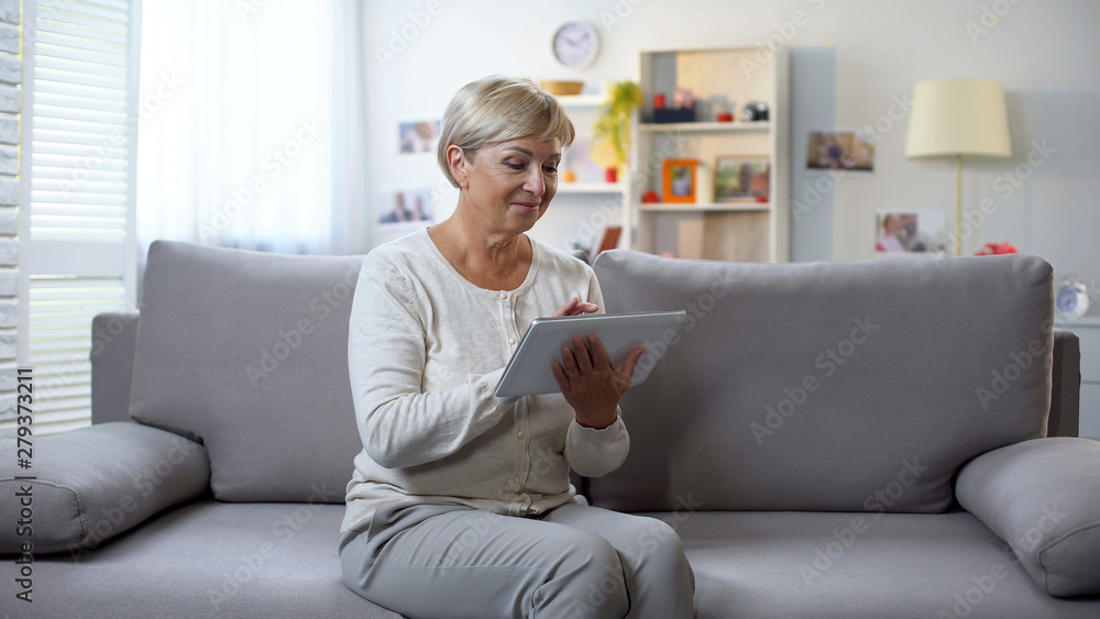 Retired female scrolling tablet application relaxing at home, shopping online Retired female scrolling tablet application relaxing at home, shopping online