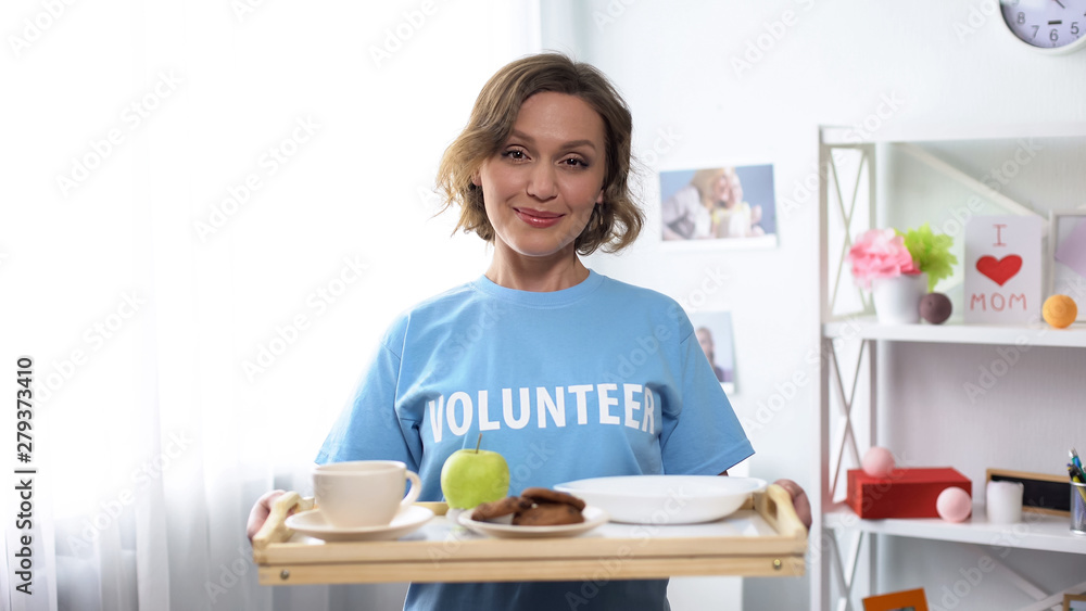 Young smiling volunteer holding tray with breakfast food in hands, kindness Young smiling volunteer holding tray with breakfast food in hands, kindness