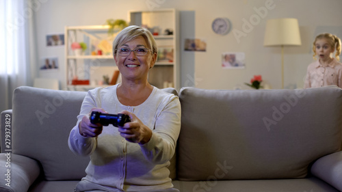 Shocked girl looking at granny playing video game on console, entertainment