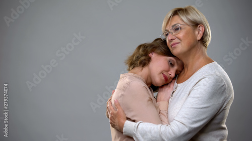 Mature woman hugging adult daughter on grey background, motherhood support