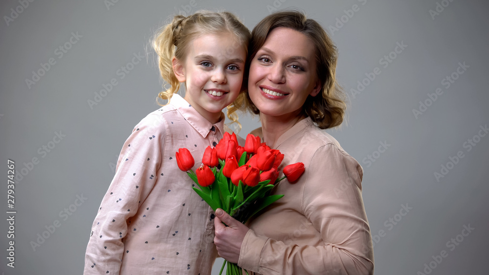 Mother and daughter hugging and looking at camera, holding flowers, mums day Mother and daughter hugging and looking at camera, holding flowers, mums day