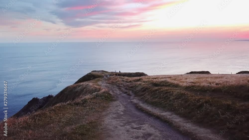 Following a footpath to the edge of the Cliffs of Moher in Ireland with the ocean and beautiful sunset in the distance Following a footpath to the edge of the Cliffs of Moher in Ireland with the ocean and beautiful sunset in the distance