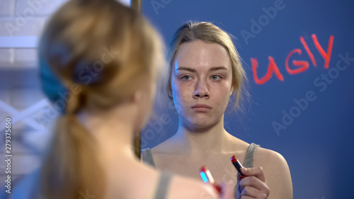 Billede på lærred Depressed girl looking in mirror, word ugly written by lipstick, insecurities