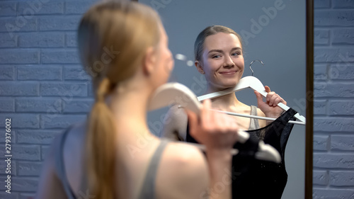 Pretty young female thinking of dress choice looking in mirror event preparation