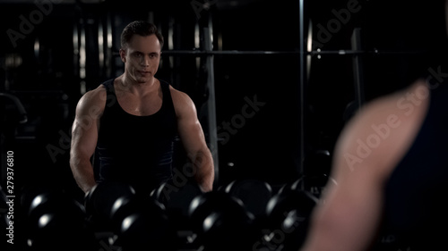 Motivated bodybuilder looking in mirror reflection during break between workouts