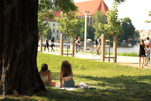Dwie młode kobiety wypoczywają pod drzewem w parku Wrocławia.