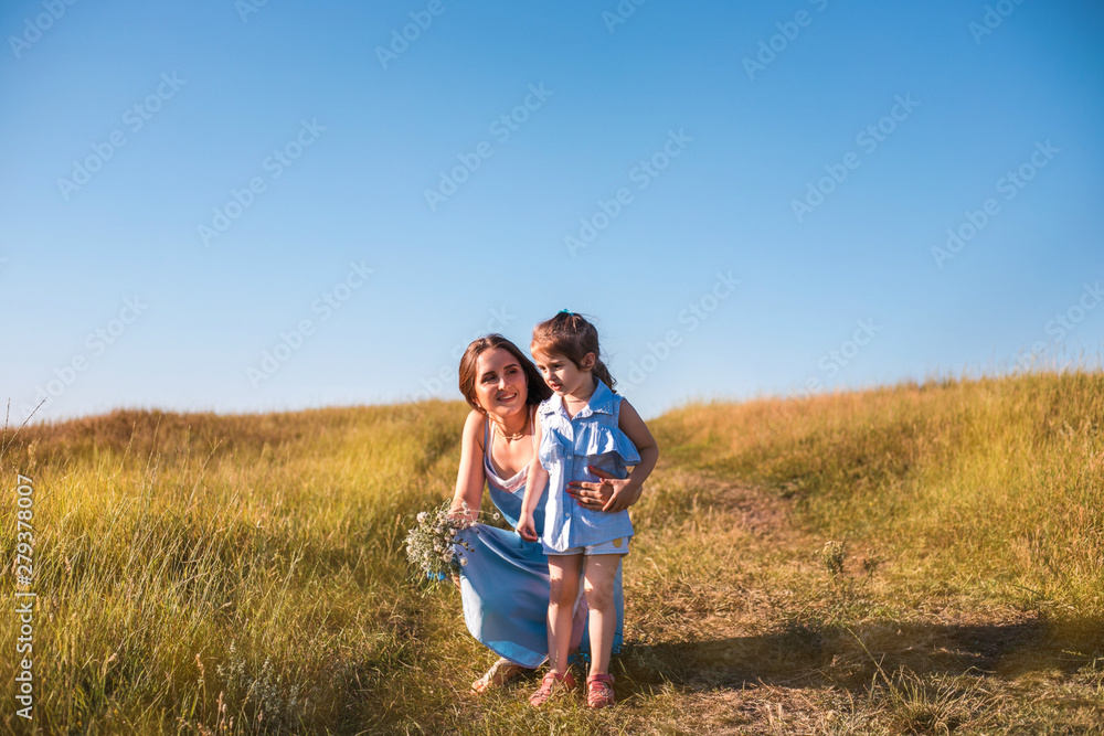 Young mother and daughter, hugging and playing in a golden field of sunshine.