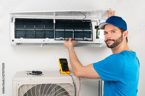 Installation service fix  repair maintenance of an air conditioner indoor unit, by cryogenist technican worker checking the air filter in blue shirt baseball cap photo