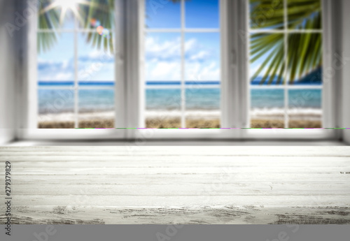 Table background with wooden top board and white window. Beautiful blurred ocean and beach view outside the window.