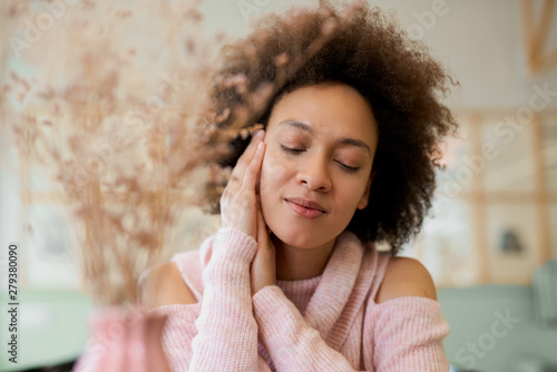 Obraz na plátně Portrait of charming mixed race woman in pink turtleneck sweater sitting in cafe