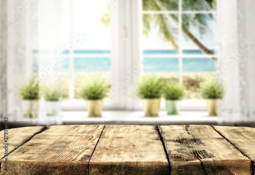 Table background with wooden top board and white window. Beautiful blurred ocean and beach view outside the window.