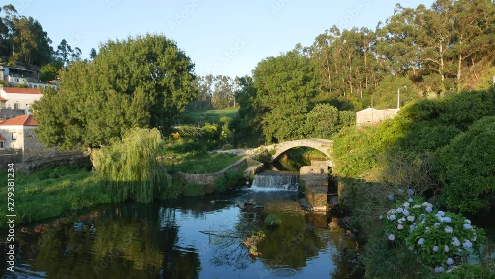 Ancient Roman stone bridge and waterfall. Overhanging weeping willow tree. River Este in Portugal. Ancient Roman stone bridge and waterfall. Overhanging weeping willow tree. River Este in Portugal.