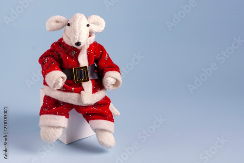 A cute white rat in a red Santa Claus suit is sitting on a white cube on a light blue background. Postcard Happy New Year 2020. Symbol of 2020 on the Eastern calendar. Copy space