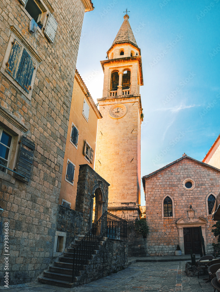 Narrow street with old historical buildings and church tower in the central district of ancient city Budva, Montenegro