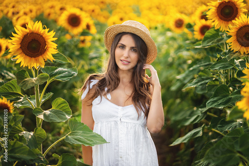 Outdoor portrait of young beautiful happy smiling girl wearing straw hat . posing at sunflower field