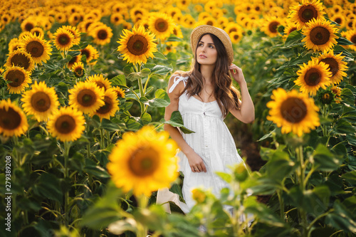 Beautiful woman in hat poses in field of sunflowers