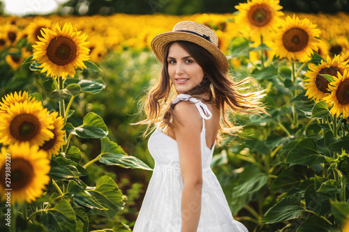 Portrait of a smiling woman in a straw hat. field with blooming sunflower at background