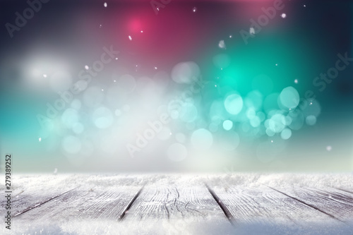 Festive Christmas stage scene background with wooden floor in snow and defocused Christmas lights. Blue and pink turquoise tones, evening, copy space.