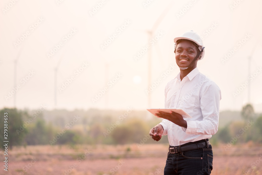 African engineer wearing white hard hat standing with digital tablet against wind turbine African engineer wearing white hard hat standing with digital tablet against wind turbine