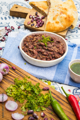 Lobio - Georgian cuisine traditional food with cooked red kidney beans, cilantro coriander and spices on Lurdji Supra tablecloth. With tkemali sauce and lobiani pie.