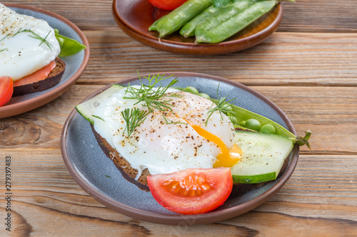 Sandwich with a poached egg and peas and tomato on a plate on wooden background