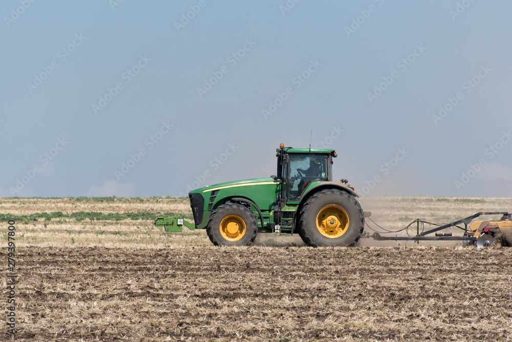 Fototapeta premium Tractor plowing the ground against the blue sky