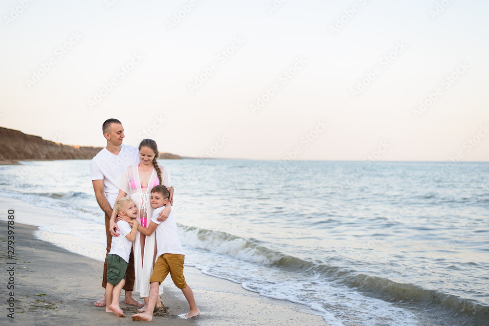 Happy family of four hugging on the sea coast. Parents, pregnant mother and two sons. Happy family of four hugging on the sea coast. Parents, pregnant mother and two sons.