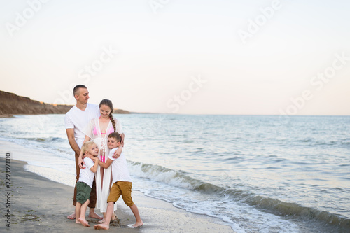 Happy family of four hugging on the sea coast. Parents, pregnant mother and two sons.