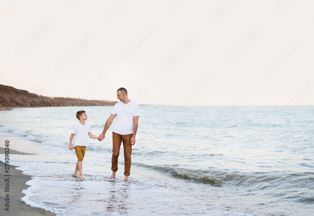 Father and son go by the hand along the sea coast. Family vacation. Friendship Father and son go by the hand along the sea coast. Family vacation. Friendship