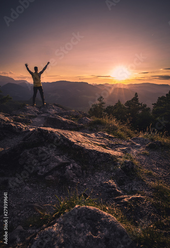 Happy man with open raised arms on the Top of a Mountain during the Sunset