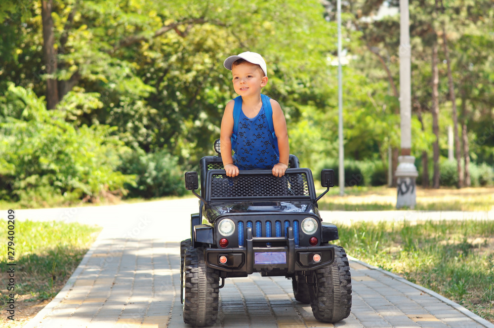 A cute, little boy drives an electric black car in a summer park. A cute, little boy drives an electric black car in a summer park.