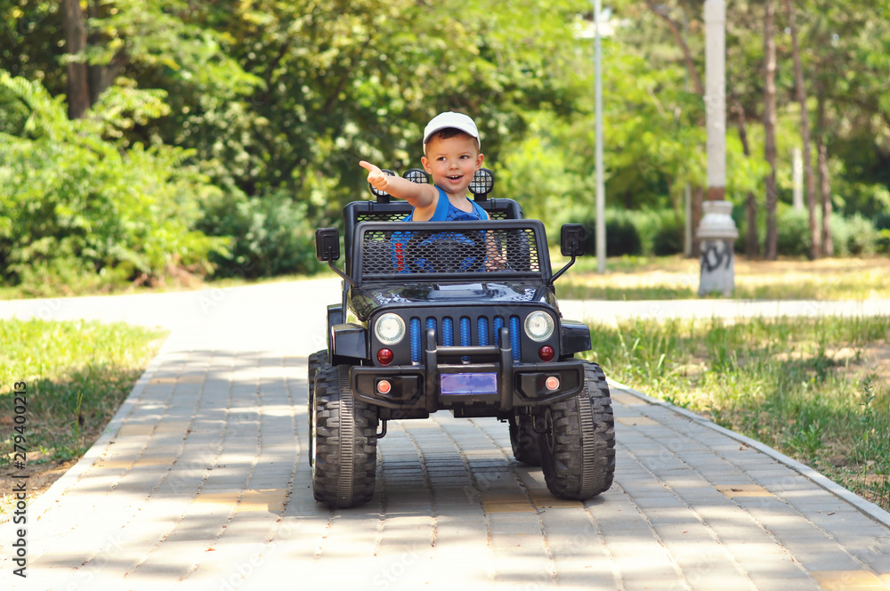 Fototapeta premium A cute, little boy drives an electric black car in a summer park. 