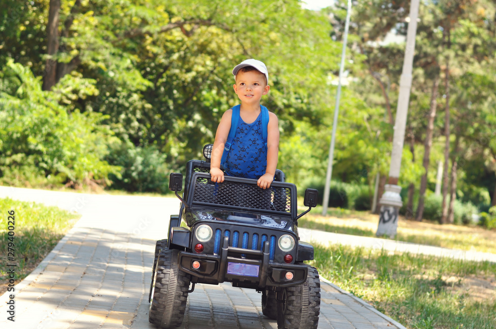 A cute, little boy drives an electric black car in a summer park.	