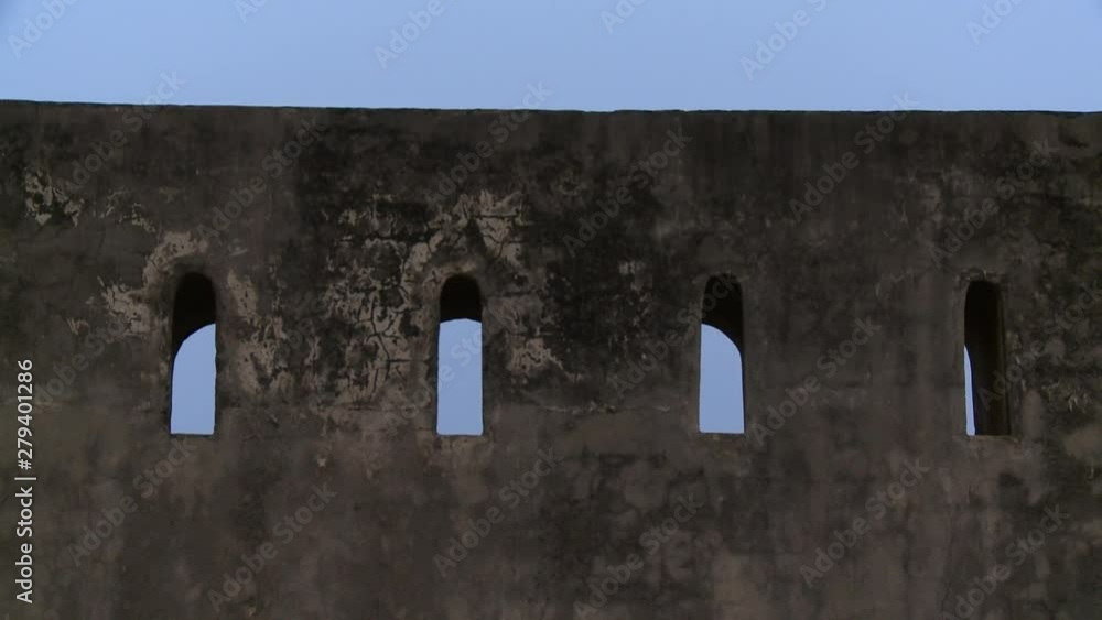A steady, close up shot of a citadel wall cracked by time with four little windows. A steady, close up shot of a citadel wall cracked by time with four little windows.