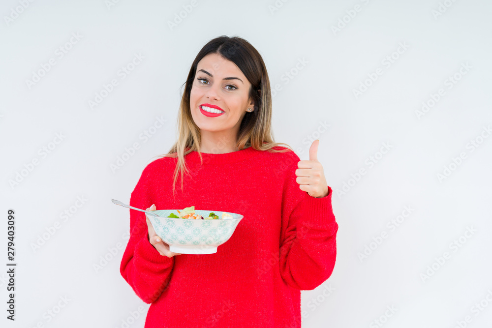 Young woman eating fresh healthy salad over isolated background happy with big smile doing ok sign, thumb up with fingers, excellent sign Young woman eating fresh healthy salad over isolated background happy with big smile doing ok sign, thumb up with fingers, excellent sign