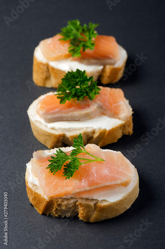 Salmon canape sandwiches with baguette on black grunge background. Canapes with smoked salmon and cream cheese. Salmon sandwich on the black background. 