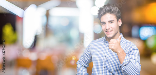 Young handsome business man over isolated background doing happy thumbs up gesture with hand. Approving expression looking at the camera showing success.