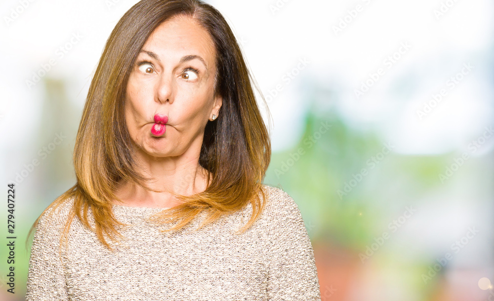 Obraz premium Beautiful middle age woman wearing fashion sweater making fish face with lips, crazy and comical gesture. Funny expression.
